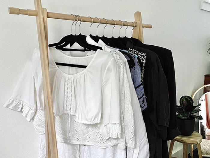 Part of my sustainable wardrobe - a partial view from the side of a wooden rack of clothing in varying shades of white, blue and black.