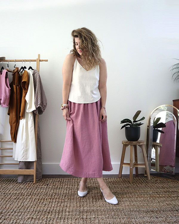 A photo of me wearing the white tank top untucked over a blush pink skirt with white slingback shoes.