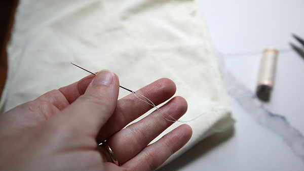 This photo shows me holding a needle with thread through the eye over the fabric that I am about to gather.