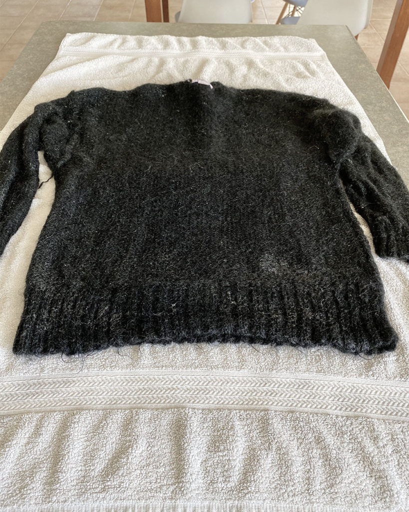 The black sweater is laid out on a white towel.