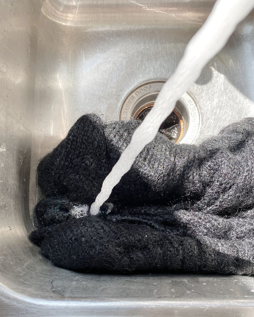 A stream of water from a tap is rinsing the black sweater.
