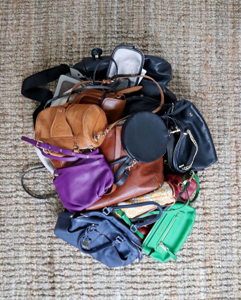 How I declutter handbags step 1. All of the handbags that I own are gathered into one big pile on a tan rug.