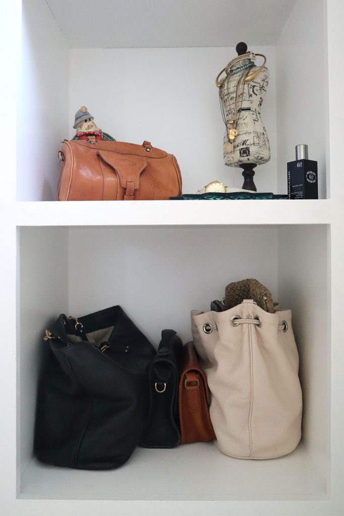A shot of the shelf that the handbags rest on. A large black one is on one end while the large white one is on the other. Two smaller satchels (black and tan) rest in the middle.