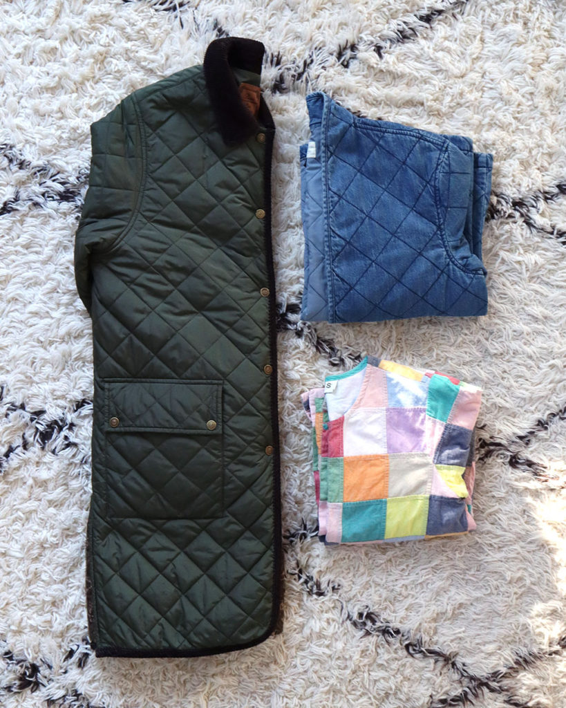 A flat lay of three quilted coats...A long green one folded in half length wise on the left and a denim one folded into a square on the right above a colorful patchwork one.