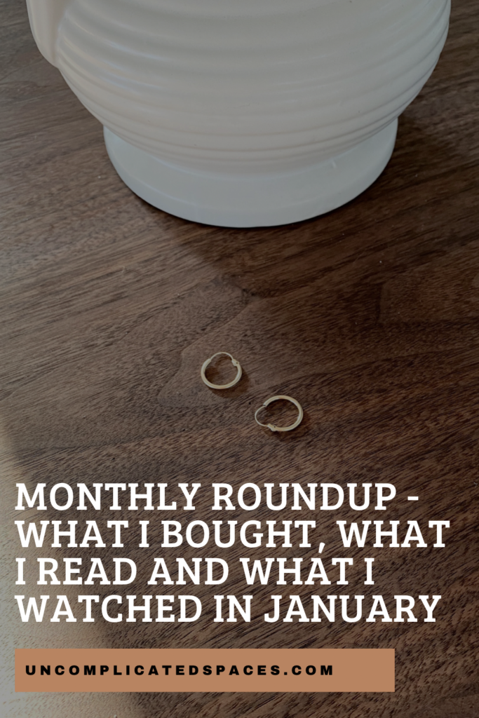 A pair of small gold hoops is laid at the base of a white vase and on top of a dark brown walnut table. You can partially see the vase and table. There is text at the bottom that reads "monthly roundup - what I bought, what I read and what I watched in January".