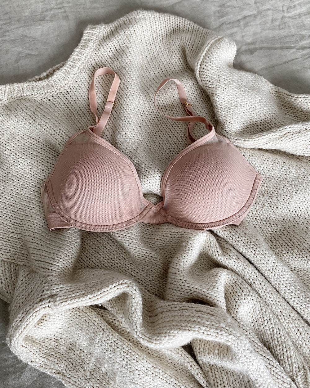 Another clothing items as part of this monthly roundup: A pair pf pink bra is laid out on top of a cream cashmere sweater.
