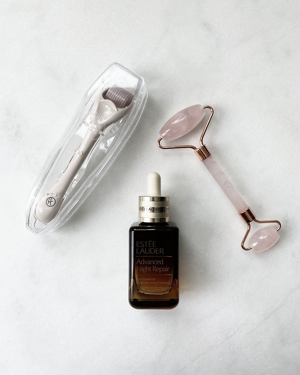 An overhead shot of a bottle of serum, a micro needle roller and a rose quartz facial roller.