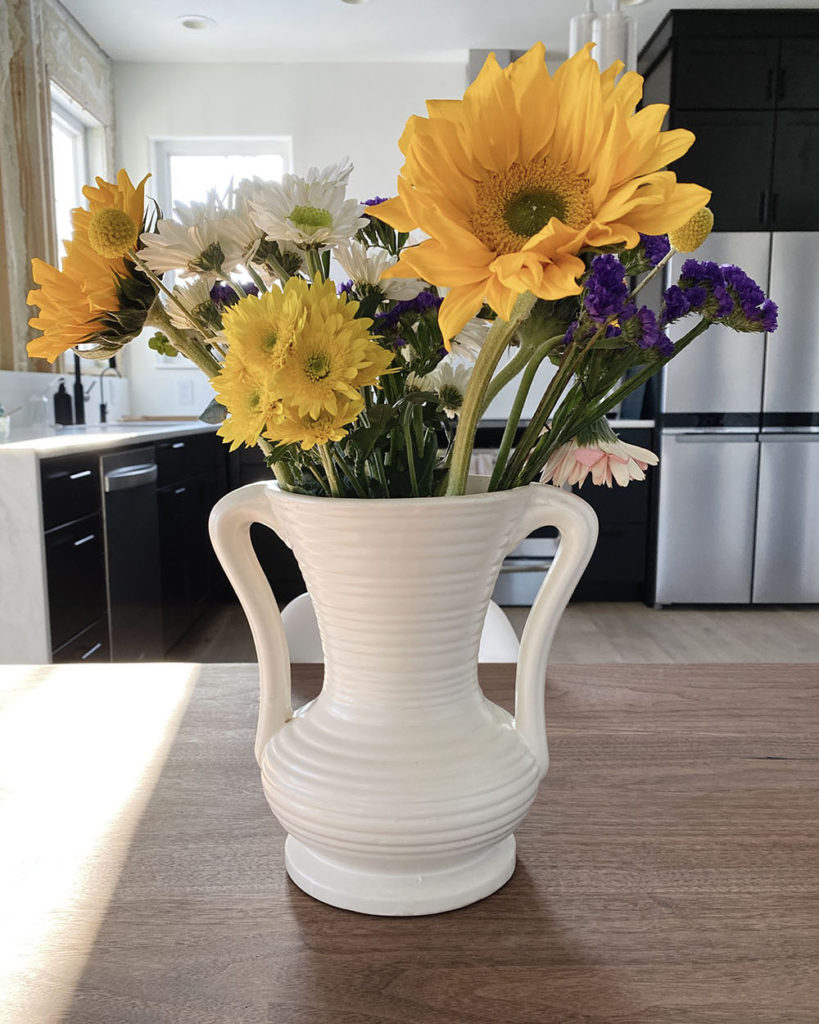 A white vase is sitting on a brown walnut tabletop and holding a bouquet of colorful flowers.