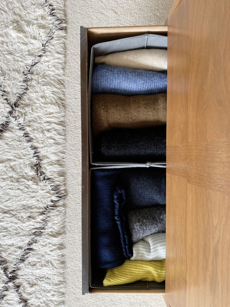 A photo shot from above of sweaters that have been rolled and placed in the bottom drawer of a dresser.