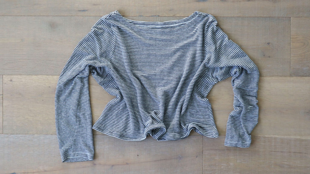 A photo from above of the final product in the experiment to crop a top. A black and white long sleeved top is semi scrunched up on a light toned wood floor.