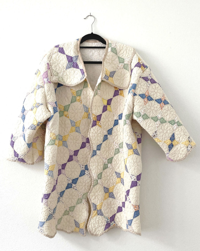 The quilted coat is hanging against a white wall. The front of the colorful side is visible.