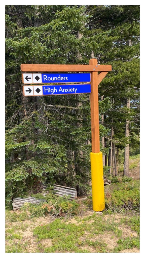 A ski sign a the top of Breckenridge ski hill. One sign points towards a trail called "Rounders" and the other one points towards a trail called "High Anxiety".