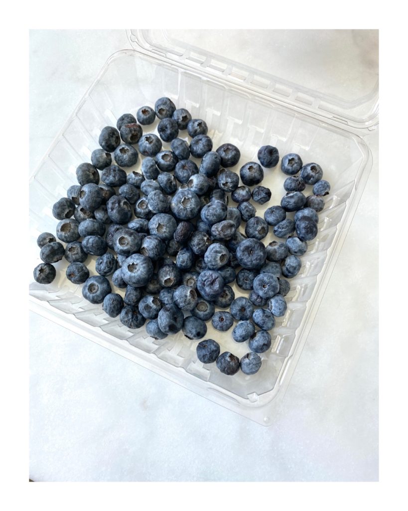 A plastic container, holding about 50 shriveled blueberries sits on a white and grey countertop.