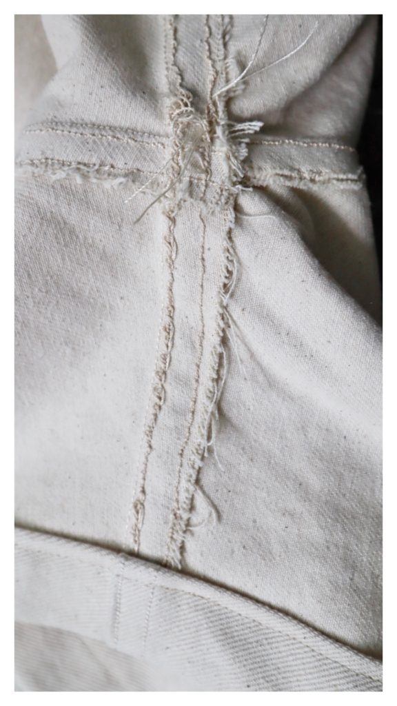 A closeup photo of an inside seam of a pair of cream colored shorts. The seam looks very messy.