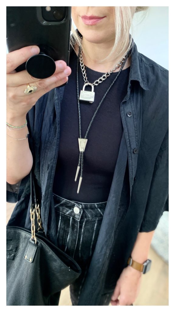 Closeup of the woman in the mirror to show the silver padlock necklace she is wearing and the black bolo tie with a silver horseshoe design.