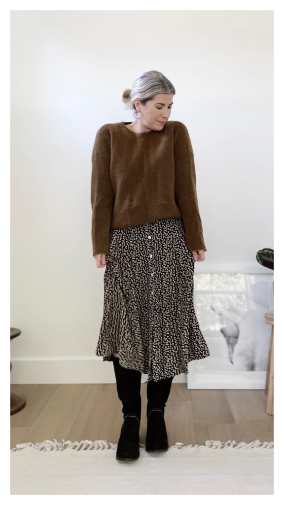 The same woman is wearing a long sleeved brown sweater over the dress. it is untucked and she is wearing it with brown slouchy boots.