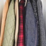 Closeup of 5 coats that are hanging in a closet. The main colors are green, red and grey.