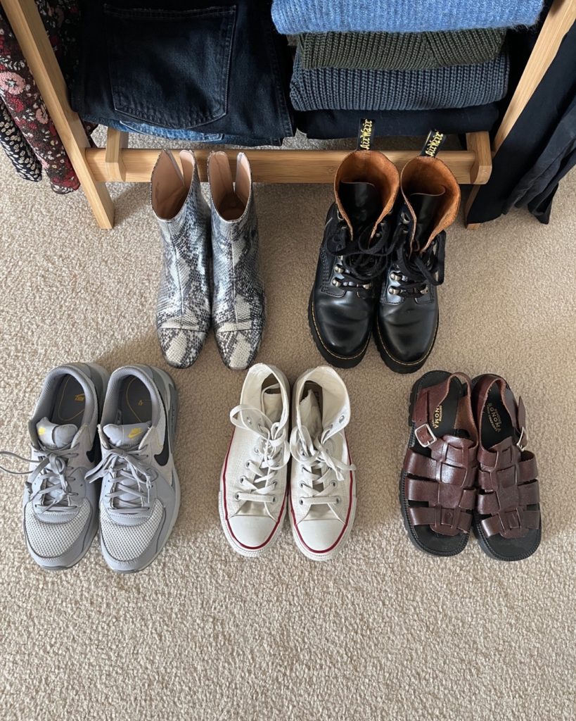 A shot from above of the shoes in my spring capsule wardrobe. They are placed in front of the wooden clothing rack. Two pairs of boots are at the back; 1 silver and 1 black. Two pairs of sneakers; 1 grey "dad" sneakers and 1 pair of white high top converse sneaker; and 1 pair of brown fishermen style sandals are in the front.