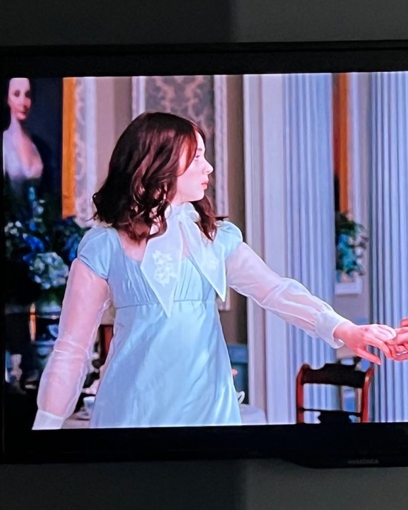 The inspiration for the mini capsule wardrobe...a picture of a tv showing a scene from the first episode of bridgerton season 2 in which the character of Eloise is wearing a light blue dress with sheer sleeves and a sheer neck tie.