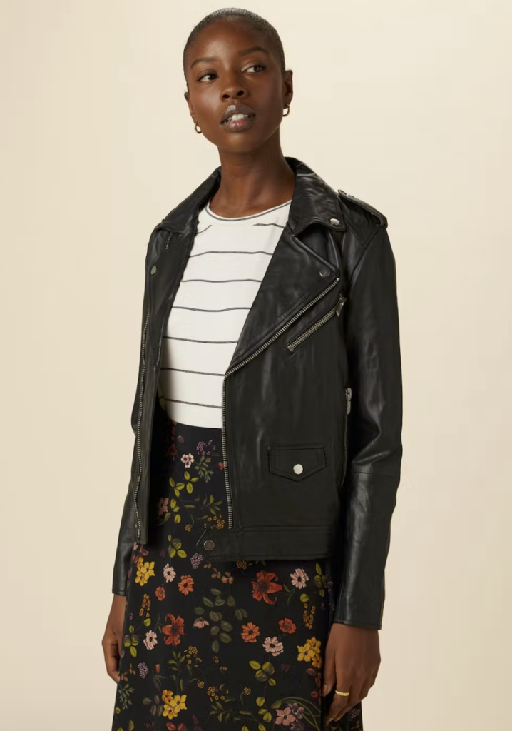 A black female model with short hair is wearing a black leather moto jacket over a white tee with slack strips and a black floral shirt. Image via Amour Vert website.