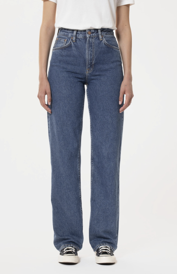 The lower portion of a white female model shows a pair of loose fitting blue jeans. The image is via the Nudie Jeans website.