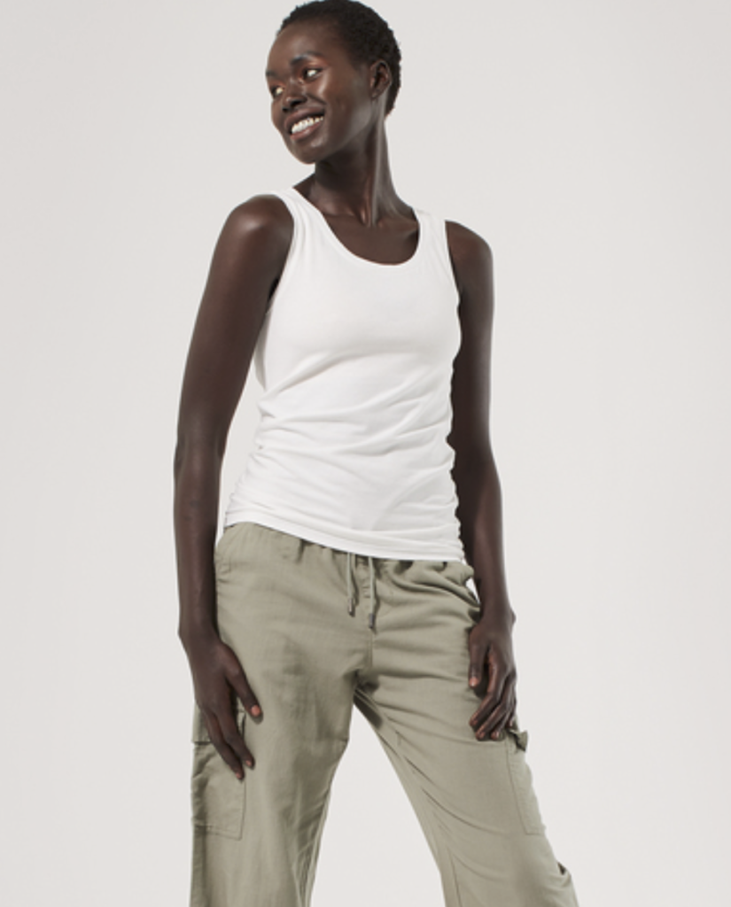 A black female model with short hair is wearing a white tank top with tan pants. Image is via the Pact website.
