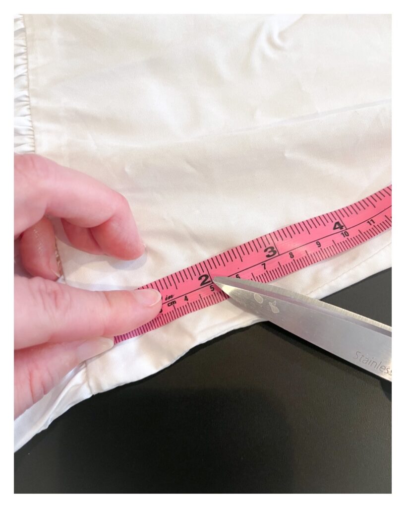 A fabric tape measure is laid on top of the dress just above the gathered waist. The tape is laid flat on the dress and the 2" mark is pointed to by a pair of fabric shears.