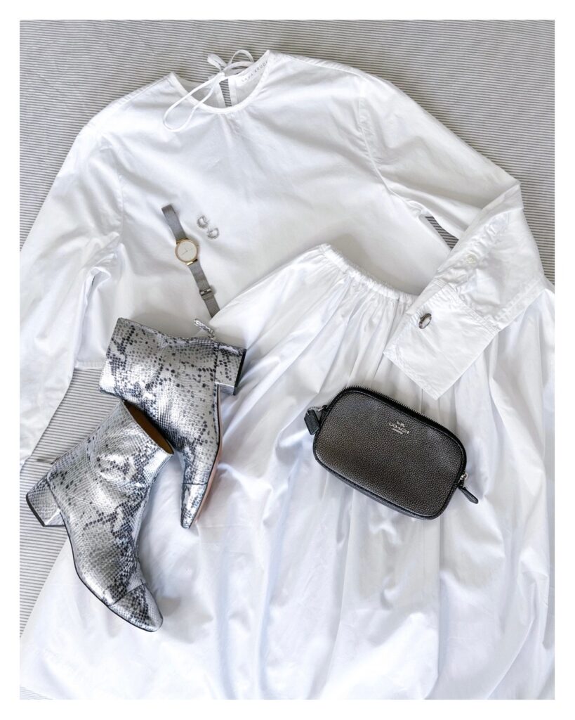 A flatlay of the matching set on a grey/white background. A small silver clutch, a pair of silver snakeskin boots, a silver watch and a pair of silver earrings are laid on top of the set. A silver cufflink is visible in one of the top's cuffs.